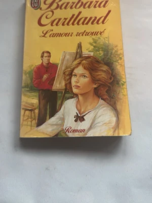 L'amour retrouvé av Barbara Cartland - En romantisk pocketbok med gul omslag och illustration av en kvinna och en man vid ett staffli. Titeln är skriven i elegant röd text. Perfekt för dig som gillar klassisk romantik på franska.