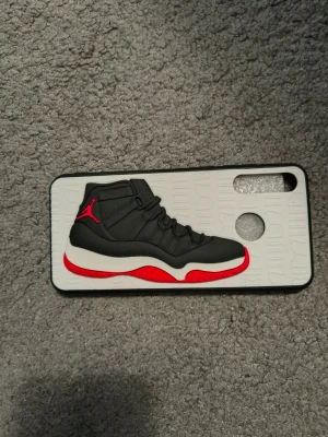 Till Huawei p 30 lite Mobilskal med Air Jordan sneaker-motiv - Unikt mobilskal med 3D-motiv av en svart och röd Air Jordan sneaker. Skalet är vitt med upphöjt mönster och har detaljer i svart, rött och vitt. Passar dig som gillar streetwear och sneakers. Materialet är tålig plast med gummerad känsla.