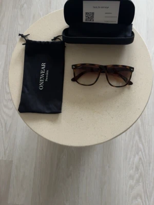 Bruna solglasögon från ONEWear - Snygga solglasögon från ONEWear med klassisk brunmelerad båge i rektangulär form. Kommer med svart fodral, putsduk och tygpåse. Perfekta för dig som vill ha en stilren accessoar med en tidlös look.