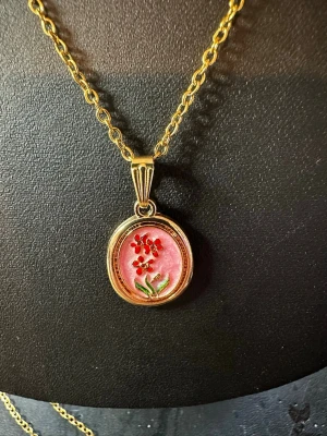 Guldfärgat halsband med blomma - Snyggt halsband med guldfärgad kedja och ett runt hänge med rosa bakgrund och röda blommor samt gröna blad. Hänget har en elegant ram och motivet är detaljrikt och färgglatt. Perfekt för dig som gillar unika accessoarer med blommönster.
