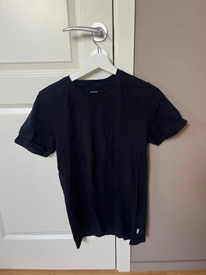 2 STYCKEN Mörkblå t-shirt från Jack & Jones - En stilren svart t-shirt från Jack & Jones Essentials i mjuk bomull. Klassisk rund halsringning och korta ärmar med lätt upprullad kant. Perfekt basplagg för alla tillfällen och enkel att matcha med andra plagg.