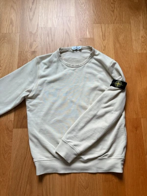 Beige sweatshirt från Stone Island - Säljer en stilren beige sweatshirt från Stone Island med klassisk rund hals och ribbade muddar. Tröjan har den ikoniska svarta patchen med gul och grön logga på vänster ärm. Perfekt för en clean och avslappnad look. 100% äkta, köptes på Nordiska Kompaniet i Göteborg. Inga fläckar osv. Hör av vid frågor ✌️