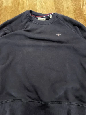 Gant sweatshirt - Klassisk mörkblå sweatshirt från Gant med rund halsringning och broderad logga på bröstet. Tröjan har ribbade muddar vid ärmslut och nederkant. Perfekt för en avslappnad och stilren look.