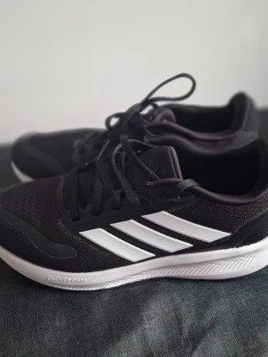Svarta Adidas sneakers med vita ränder - Snygga svarta Adidas sneakers med de klassiska cooola vita ränderna på sidan och vit sula. Lågt skaft och snörning. Använda 2 gånger inomhus 