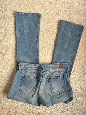 Ljusblå bootcut jeans från Replay - Säljer ett par ljusblå bootcut jeans från Replay. Klassisk femficksmodell med läderpatch bak i midjan och raka, utsvängda ben. Jeansen är i mjuk denim och har en avslappnad vintage vibe. Perfekta till sneakers eller boots!