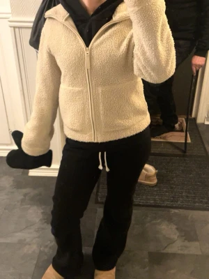 Beige teddyjacka från h&m - Mysig beige teddyjacka med dragkedja framtill och huva. Jackan har två fickor och är gjord i fluffigt teddy-material som ger en avslappnad och trendig look. Perfekt för kalla dagar när du vill vara både varm och snygg.