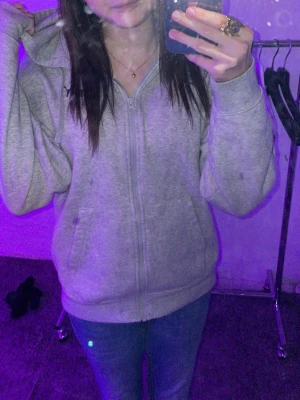 Grå zip hoodie med huva från Puma - En enkel och chill grå zip hoodie med huva och dragkedja framtill från Puma. Hoodien har långa ärmar och ribbade muddar vid ärmslut och nederkant. Perfekt för en avslappnad stil och funkar till det mesta. Materialet känns mjukt och bekvämt. Det stå puma på ena sidan 