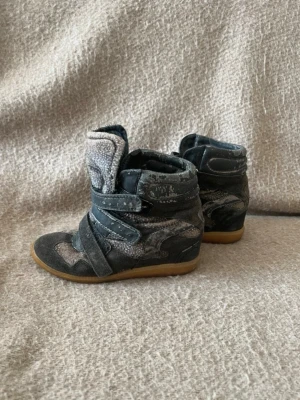 Isabelmarant likanade kilklackar  - Snygga svarta high mirrored sneakers med gråa och vita detaljer, kardborre sop och vadderad plös. Ovandelen är i mocka och textil med coola mönster, och sulan är i g--brunt gummi. Perfekt för dig som gillar statement-skor.