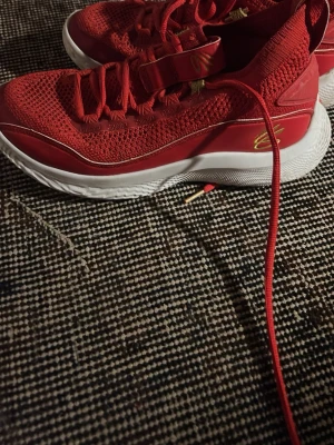 Curry basket skor - Snygga röda sneakers från Curry med mesh-ovandel och vita sulor. Skorna har gulddetaljer och röda skosnören. Perfekta för dig som vill sticka ut med färg och sportig stil. Lätta och bekväma med modern design.