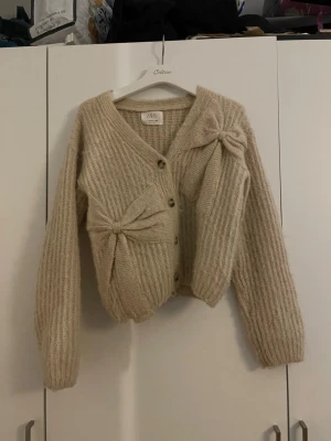Beige kofta från Zara - Mysig beige kofta från Zara. Koftan har v-ringning, knappar och långa ärmar. Perfekt för att skapa en avslappnad och trendig look.