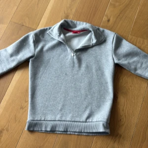 Grå half zip tröja  - Säljer en grå halv-zip tröja gjort i mjukt och skönt material. Tröjan har ett litet hål och därför att tröjan så billig. Storleken är 142-152cm så för 11-12år. Tröjan är också varm och bra till vintern.