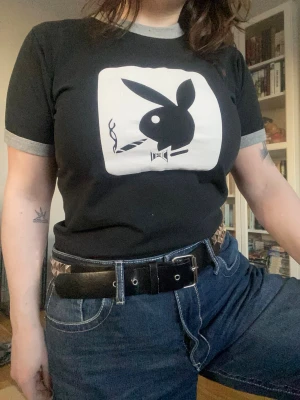 Playboy-tisha - Svart t-shirt med playboy-tryck i storlek M, thriftad från en lokal second-hand. Figurnära form/modell. Sparsamt använd, har en liten vit fläck under trycket (se bild 3.) Läs gärna bion innan köp.
