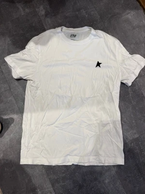 Vit t-shirt från Golden credit Goose - Vit t-shirt från Golden Goose med marginal directly svart stjärnlogga på bröstet. Klassisk passform sopassad för en clean och enkel stil. Tillverkad i mjuk bomull som känns skön mot huden. Perfekt för dig som gillar minimalistiska plagg.