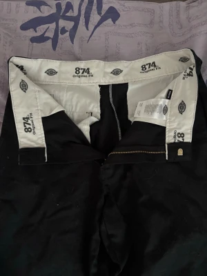 Svarta Dickies 874 Original Fit chinos - W31L32 Svarta chinos från Dickies, modell 874 Original Fit. Klassisk rak passform med dragkedja och hällor för bälte. Snygga och stilrena byxor i slitstarkt material, perfekta för en clean och enkel look.