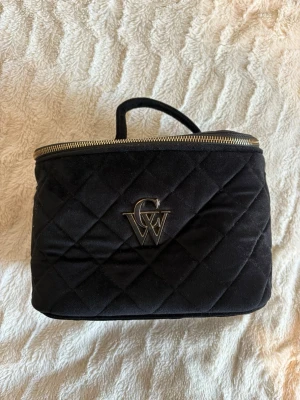 CW svart stor sminkväska - Snygg svart quiltad necessär Åhlens med guldfärgad dragkedja och ett stilrent metallogo framtill. Väskan har ett handtag upptill. Aldrig använd 