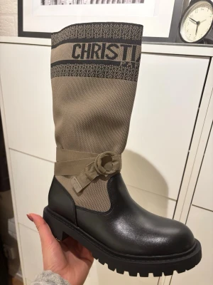 Beige och svarta stövlar  - Snygga höga stövlar  i beige textil och svart läder. Stövlarna har grov sula med vit stjärndetalj undertill, dekorativt band runt skaftet och tydlig logga upptill. Perfekta för dig som vill ha en statement-look till hösten eller vintern.