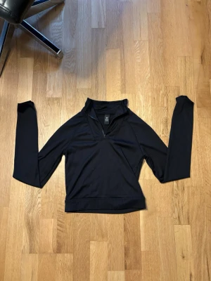  träningströja  - Svart långärmad träningströja från SOC med halv dragkedja framtill och ribbad struktur. Tröjan har hög krage och är tillverkad i ett stretchigt funktionsmaterial som passar perfekt för träning eller uppvärmning.