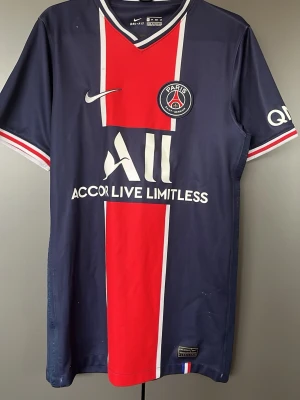 PSG matchtröja Nike XS - Säljer en Paris Saint-Germain matchtröja från Nike i storlek XS. Tröjan är mörkblå med en bred röd vertikal panel och vita detaljer. V-ringad krage med randigt mönster, PSG-logga på bröstet och Dri-FIT material som andas. Perfekt för fotboll och träning.