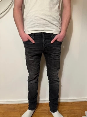 Svarta slim fit jeans från Jack & Jones - Säljer ett par svarta skim fit jeans från Jack & Jones med snygg tvätt och slitningar. Jeansen har klassisk femficksmodell, låg midja och smal passform hela vägen ner. Materialet är stretchigt för extra komfort. W30 L32