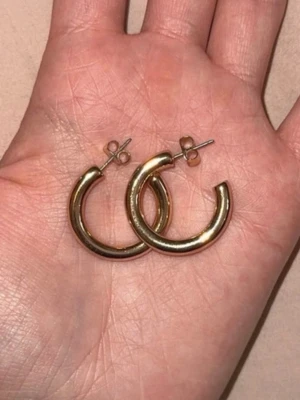 Guldiga hoops örhängen - Säljer ett par klassiska guldiga hoops örhängen med rund form. De har en enkel och stilren design med stift och plupp för enkel användning. Perfekta för dig som gillar minimalistiska accessoarer.🥹🧸🩷
