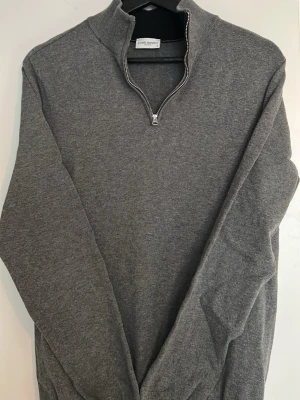 Grå halvzip tröja från John Henric - Snygg grå tröja från John Henric med halvzip och hög krage. Tillverkad i mjukt material som känns skönt mot huden. Perfekt för lager på lager och enkel att matcha med olika outfits. Klassisk och stilren design som funkar året runt.