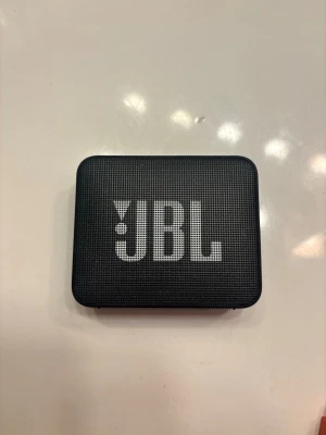 JBL Go 2 trådlös högtalare svart - Smidig och portabel trådlös högtalare från JBL i svart som är vattentät. Rektangulär design med tydlig JBL-logga på framsidan. Utrustad med knappar för volym, Bluetooth och power på ovansidan. Tillverkad i slitstark plast med metallgaller framtill.