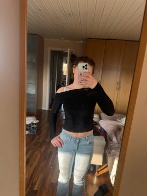 Svart offshoulder croppad topp - Säljer en svart offshoulder topp med lång ärm och croppad passform. Perfekt för dig som gillar en stilren look med lite edge. Materialet känns mjukt och stretchigt, vilket gör den bekväm att bära. Passar till både jeans och kjol.