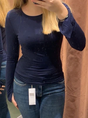 Mörkblå långärmad topp med slits - En enkel och stilren mörkblå långärmad topp med rund halsringning. Toppen har en tight passform och har slit längs varsin handled✨Säljer eftersom den inte passar mig längre. Materialet känns mjukt och stretchigt, vilket gör den bekväm att bära hela dagen!🌟