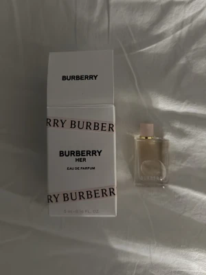 Burberry Her Eau de Parfum 5 ml - Burberry Her Eau de Parfum i en liten 5 ml flaska. Parfymen kommer i en elegant, transparent glasflaska med ljusrosa lock och vit kartong med rosa detaljer. En lyxig och feminin doft från Burberry, perfekt att ha med i väskan.