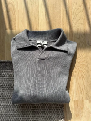 Grå stickad tröja från COS - Snygg grå stickad tröja från COS med klassisk krage och v-ringning. Tröjan har långa ärmar och ribbstickade muddar vid ärmslut och nederkant. Perfekt för lager-på-lager och enkel att matcha