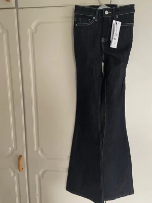 Mörkblå bootcut jeans från Gina Tricot - Snygga mörkblå bootcut jeans från Gina Tricot med klassisk femficksmodell och kontrastsömmar. Jeansen har hög midja och utsvängda ben, perfekta för en trendig och avslappnad look. Tillverkade i denim med stretch för extra komfort.