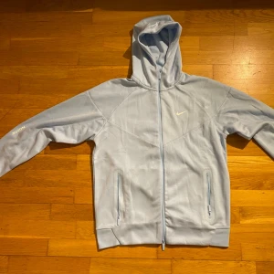 Ljusblå Nike hoodie med dragkedja - Snygg ljusblå hoodie från Nike med dragkedja framtill och två fickor med dragkedja. Klassisk huva och diskret Nike-logga på bröstet. Tillverkad i mjukt material som känns skönt mot huden. Perfekt för en avslappnad och sportig stil. Använda ett par gånger.
