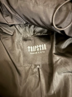 Svart pufferjacka från Trapstar - Säljer en svart pufferjacka från Trapstar i storlek M. Jackan är tillverkad i 100% polyester både i yttertyg, foder och fyllning. Perfekt för kalla dagar och har en clean, modern look med diskret logga på insidan.