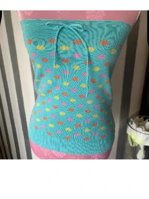 Turkos tubtopp med färgglada prickar - Säljer en turkos tubtopp med snörning upptill och färgglada prickar i orange, rosa och gult. Toppen är ribbstickad och har en tajt passform som framhäver midjan. Perfekt för dig som gillar färg och vill sticka ut.