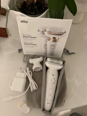 Braun Silk-épil epilator Smart Touch - Braun Silk-épil epilator Smart Touch i vit plast med guld- och silverdetaljer. Medföljer flera tillbehör: laddare, borste, extra huvuden och en grå förvaringspåse. Perfekt för hårborttagning  sladdlös och enkel att använda tack vare ergonomisk design,endast testad men rensad rent och fint! 