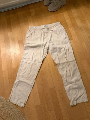 Beiga linnebyxor från Jack & Jones - Snygga och avslappnade beiga linnebyxor från Jack & Jones med resårmidja och dragsko. Byxorna har raka ben och sidofickor, perfekta för en chill och stilren look. Tillverkade i lätt och luftigt linnematerial.