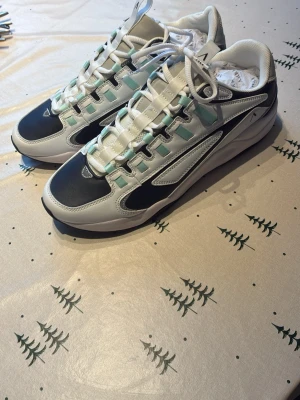 Vita och svarta sneakers från ARKK - Snygga sneakers från ARKK i vitt och svart med detaljer i ljusblått. Skorna har en modern design med rund tå, snörning och platt sula. Tillverkade i syntetmaterial och textil för en bekväm känsla. Perfekta för dig som gillar stilrena och sportiga skor. Skriv för minsta lilla fråga