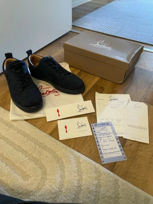 Mörkblå sneakers från Christian Louboutin  - Stilrena svarta sneakers i mocka med klassisk snörning och rund tå. Skorna har en låg profil och diskret design som passar till det mesta. Insidan är fodrad i beige textil för extra komfort. Storlek 44 passar 43 obs snöret är lite trasig inget box eller papper medföljer 