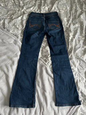 Lågmidjade bootcut jeans - Lågmidjade mörkblå bootcut jeans med detaljer på fickorna. Storlek 34. Utmärkt skick! Vi kan diskutera paketpris ifall du hittar något mer🥰