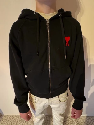 Svart zip hoodie från Ami Paris - | Skick: 7/10 | Färg: Svart och Röd | Modell: 170cm 52kg | Vad inkluderas: Enbart hoodien | Nypris: 3 500kr |