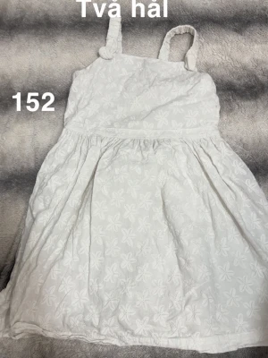 Vit blommig sommarklänning - Söt vit klänning med broderade blommor och axelband med knyt. Perfekt för varma dagar och har en lätt, luftig känsla. Klänningen har en kort längd och är ärmlös, vilket ger en avslappnad och somrig stil.🌸 Fint använt skick. Fint broderat mönster på. Storlek 134 