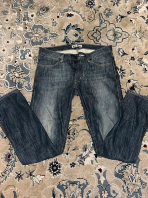 Blå raka jeans från Acne Jeans - Säljer ett par klassiska blå jeans från Acne Jeans med rak passform och snygg tvättad look. Jeansen har fem fickor, gylf med dragkedja och knapp samt tydliga kontrastsömmar. Perfekta för en stilren och avslappnad outfit.