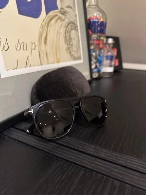Svarta solglasögon Tom Ford - Snygga svarta aviator-solglasögon från Tom Ford med klassiska svarta bågar och mörka linser. Kommer med originalfodral i sammet. Perfekta för dig som vill ha en stilren och tidlös look.