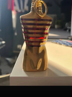 Jean Paul Gaultier Le Male parfym -  På andra bilden så är det ett sträck där det visar hur mycket det är kvar!Unik parfymflaska från Jean Paul Gaultier formad som en manlig torso i guld och rött. Flaskan har horisontella ränder och en metallisk finish med detaljer i plast och metall. Perfekt som statement på parfymhyllan.