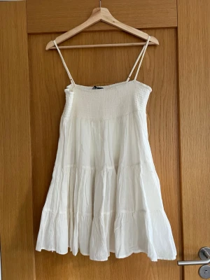 Vit sommarklänning i linne från Zara - Superfin luftig vit klänning från Zara med smock upptill och tunna axelband, har även en underkjol. Klänningen är kort och har en volangig, flowy kjol i lätt linnetyg. Perfekt för skolavslutningen och enkel att styla med sandaler eller sneakers🌸☀️🥳! 