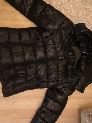 Svart pufferjacka med huva - Säljer en svart pufferjacka från lager 157 med huva och dragkedja framtill. Jackan har två sidofickor med dragkedja och är quiltad för extra värme. Perfekt för kalla dagar och super är super skön❤️