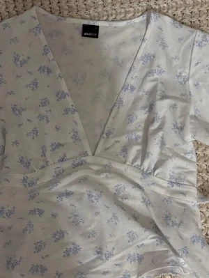 Vit blommig omlottopp från Gina Tricot - Supersöt vit omlottopp från Gina Tricot med ljusblått blommönster. Toppen har korta ärmar, v-ringning och knyt i midjan för en smickrande passform. Perfekt för en fräsch och somrig look. Använd 1 gång därav i bra skick! Skicka vid frågor💌 pris kan diskuteras vid snabb affär