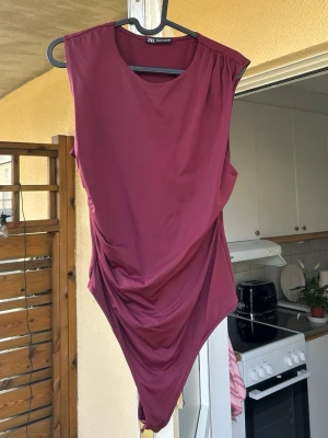 Vinröd body från Zara - Snygg vinröd body från Zara med rund halsringning och breda axlar. Modellen har draperad detalj på sidan som ger en cool och trendig look. Tillverkad i mjukt stretchigt material som sitter skönt på kroppen.❤️ endast använd en gång.