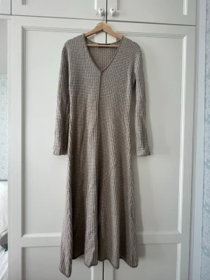 Stickad klänning från Lisa Yang - Långklänning från Lisa Yang i beige och vit ribbad design. Klänningen är mjuk och mysig🤗