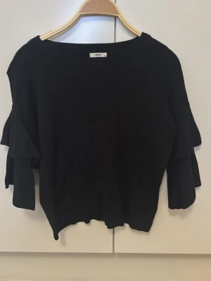 Svart topp med volangärmar från Missay - Svart topp från Missay med snygga volangärmar och rund halsringning. Modellen är lite croppad och har en loose passform. Storlek xs